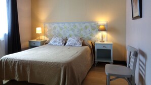 Une chambre à coucher bien rangée, avec un lit, deux tables de chevet dotées de lampes, une chaise et un tableau encadré au mur.