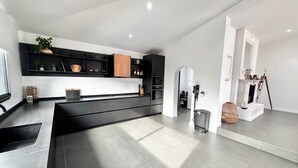 A modern kitchen with dark cabinetry, a central island, and a dining area with a white table and chairs.