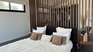 A modern bedroom with a large bed, wooden slats, a bedside table, and a view of the outdoors.
