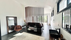 A modern living room with a sofa, a chair, a large mirror, and a sliding glass door leading to an outdoor area.