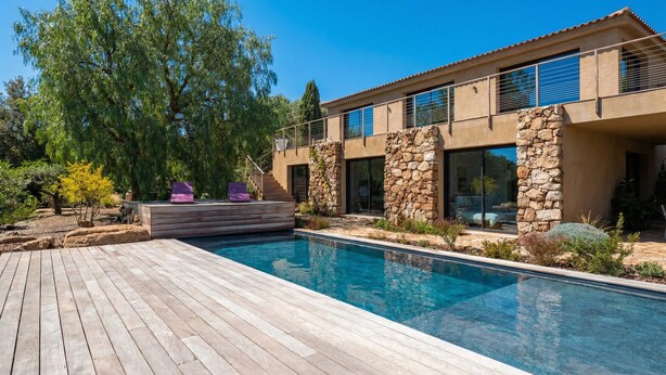 A modern house with a swimming pool, stone walls, and a wooden deck.