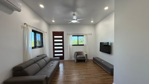 Ein modernes Wohnzimmer mit einer Couch, einem Sessel, einem Fernseher und einem Deckenventilator.