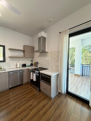 Una cocina moderna con lavavajillas, horno y microondas, armarios de madera y vistas a un balcón.