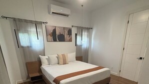 Ein Schlafzimmer mit Bett, Holzboden, Deckenventilator, Klimaanlage und einer Tür.