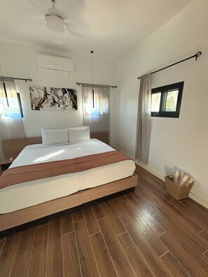 Une chambre à coucher avec un lit, des rideaux, une fenêtre et un climatiseur fixé au mur.