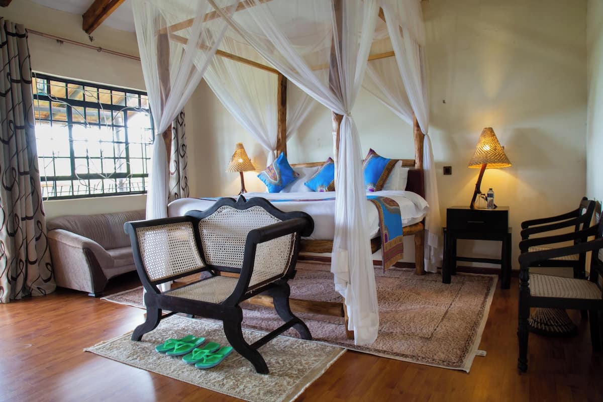 A bedroom with a four-poster bed, a chair, a small table, and a nightstand.
