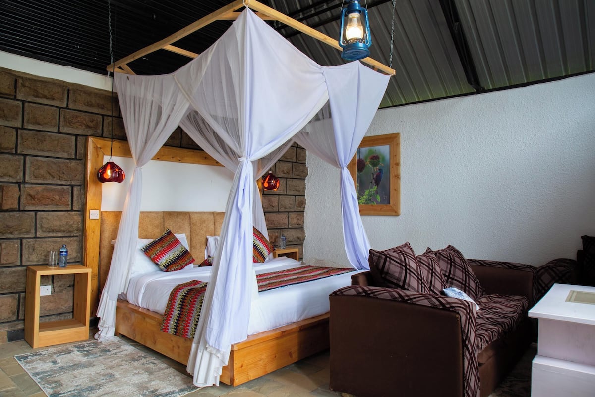 A room with a four-poster bed, a wooden nightstand, a brown sofa, and a white table.