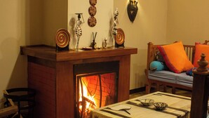 A cozy living room with a fireplace, a wooden bench, and a table with cutlery. - Saba House & Lodges (Machakos)