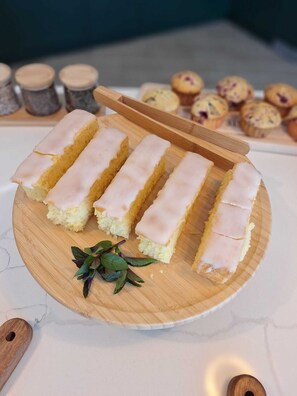 A wooden board with several slices of cake topped with white icing, a small bunch of green leaves, and a wooden spoon. - Quinta D'Joanes Douro (Resende)