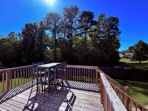 A wooden deck with a table and chairs, surrounded by a wooden fence and trees.
