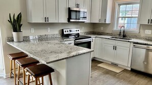 A modern kitchen with white cabinets, a granite countertop, a stainless steel stove, and a large island with bar stools.