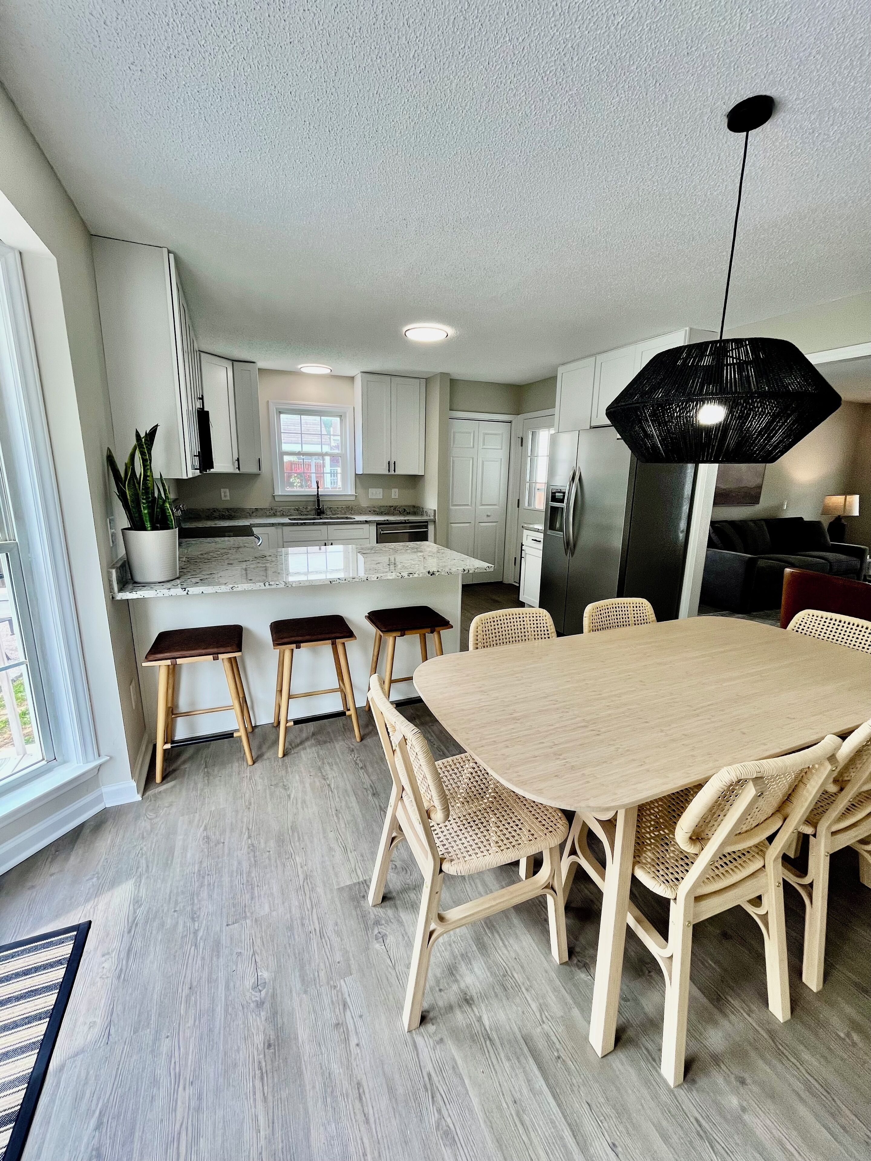 A modern kitchen with white cabinets, a central island, and a dining area with a wooden table and chairs.