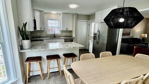 A modern kitchen with white cabinets, a central island, and a dining area with a wooden table and chairs.