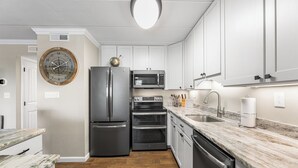 A modern kitchen with white cabinets, stainless steel appliances, a wooden floor, and a marble countertop. - Sea Winds North 112, North OC, Close to the Beach (Ocean City)