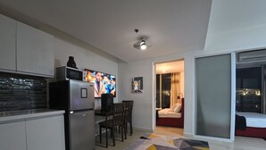 Eine moderne Küche mit integriertem Kühlschrank, einem Flachbildfernseher und einem Essbereich mit Tisch und Stühlen. Auf dem Boden liegt ein Teppich mit Muster, und eine Schiebetür führt in ein Schlafzimmer.