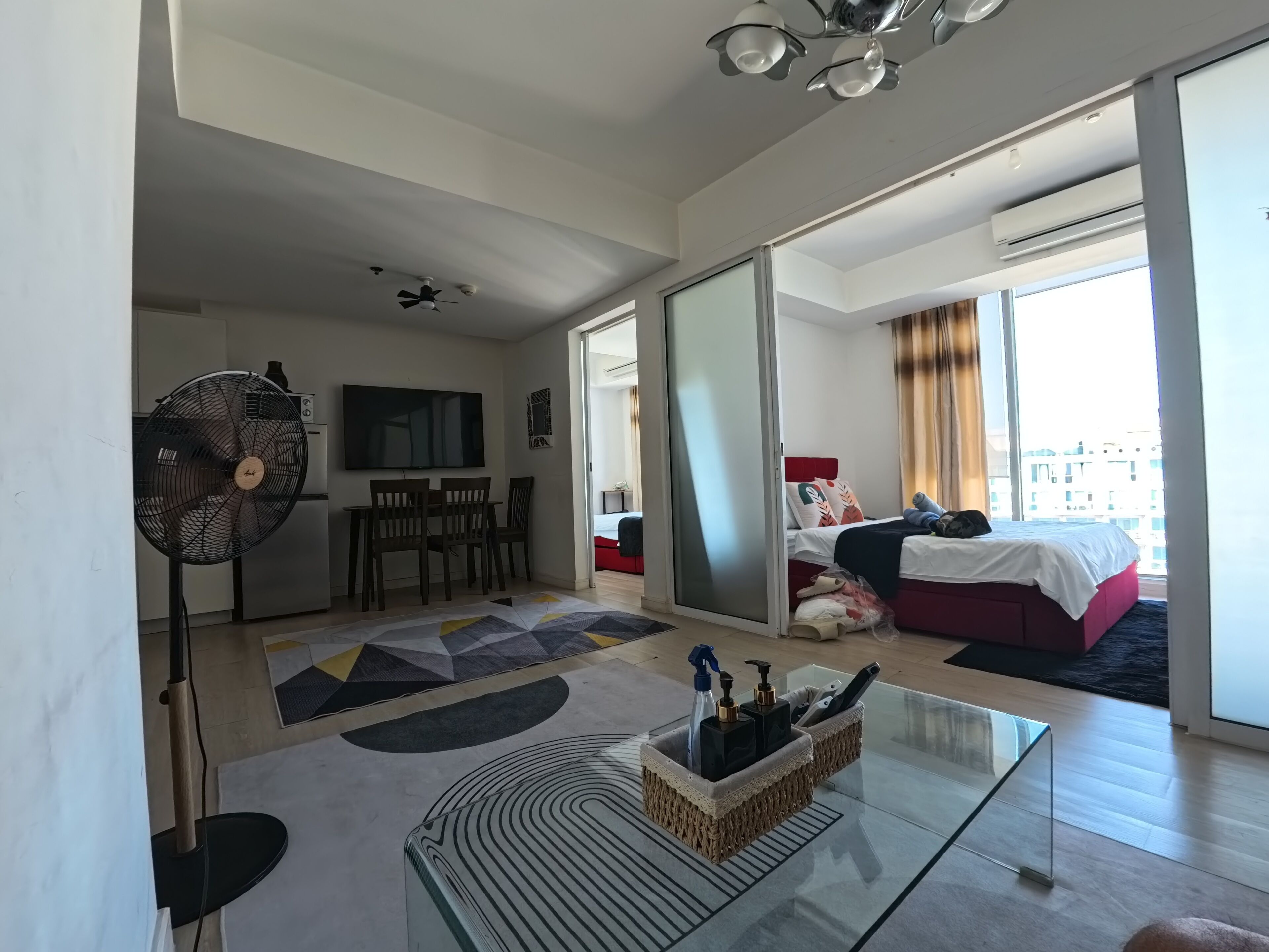 A modern hotel room with a dining area, a bed with a view, and a glass coffee table with toiletries.