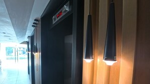 Ein Flur mit einer digitalen Uhr, die 16:16 anzeigt, einer Reihe schwarzer Pendelleuchten und einer Wand aus Holzpaneelen.