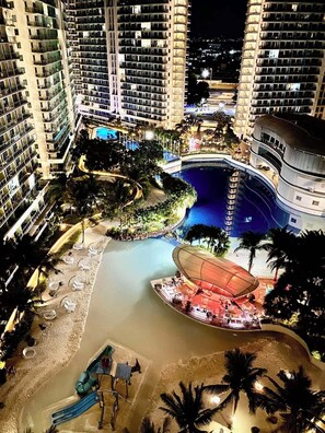 Un hôtel de grande hauteur doté de nombreux balcons, d’une piscine centrale et d’un espace plage avec des chaises longues et un toboggan aquatique.