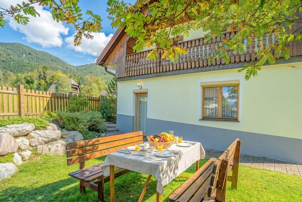 Ein zweistöckiges Chalet mit Balkon, einem gedeckten Esstisch mit Frühstück und einer Steinmauer im Hintergrund.
