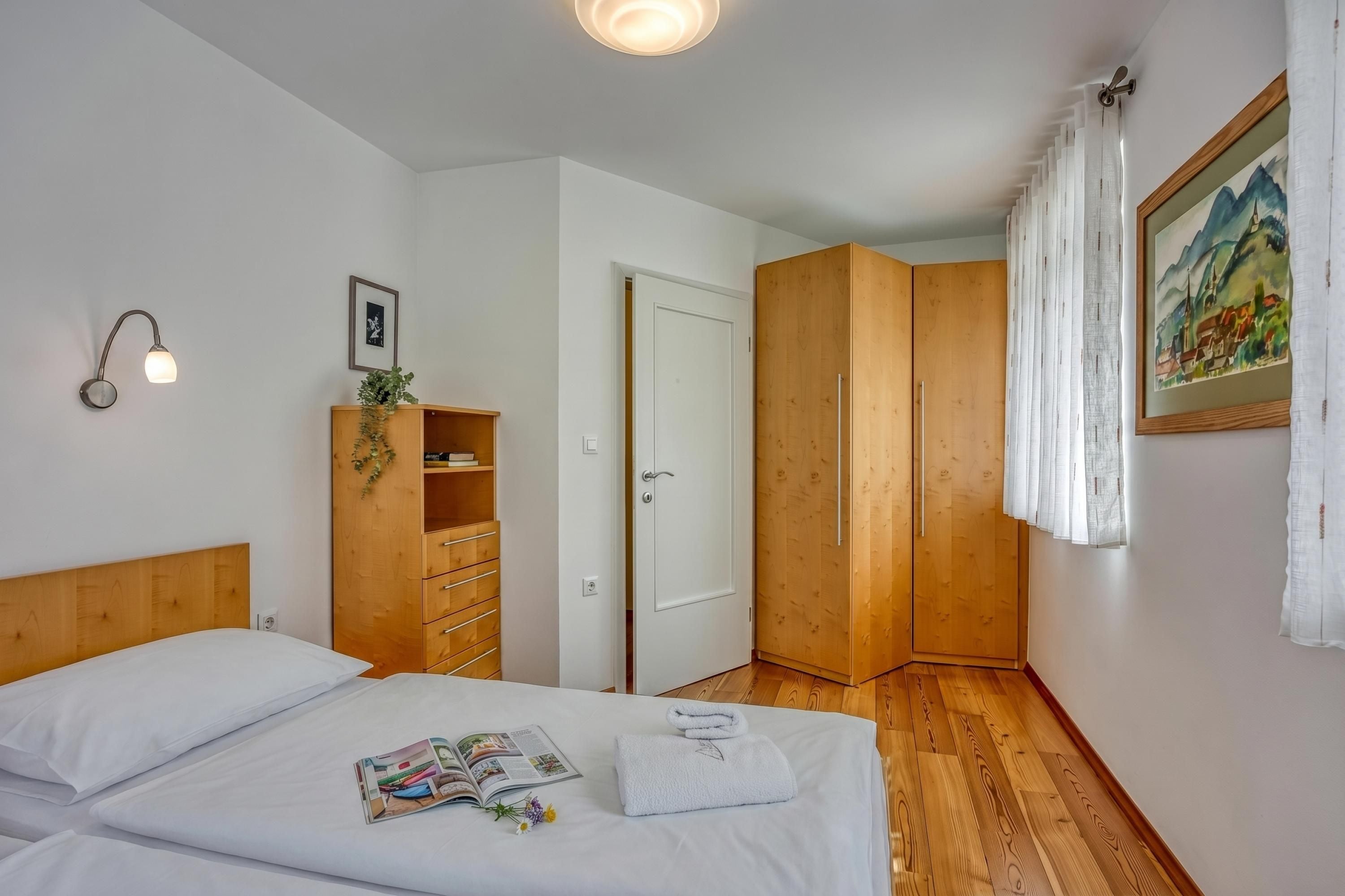 A bedroom with a wooden headboard, a bedside table with a lamp, a wardrobe, a door, and a painting on the wall.