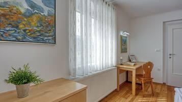 A room with a wooden desk, a chair, a radiator, a potted plant, and a painting on the wall.