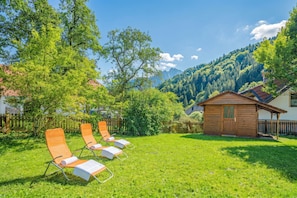 Un espace verdoyant avec quatre chaises longues, un chalet en bois et une chaîne de montagnes en arrière-plan.
