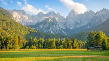 Un paysage montagneux, avec un ciel dégagé, un champ herbeux et une petite construction au premier plan.