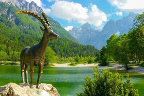 A mountain goat statue by a lake with a forest and mountains in the background.
