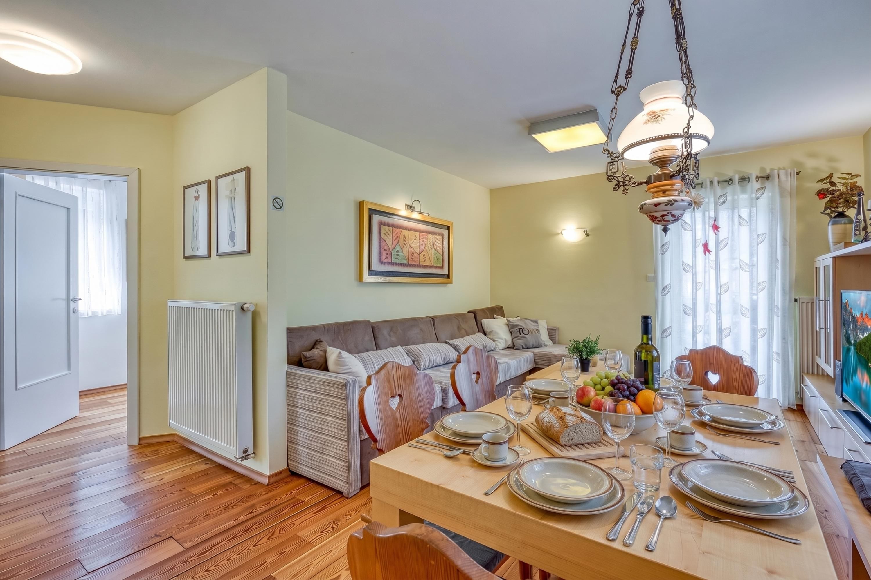 A dining area with a wooden table set for a meal, a sofa, a radiator, and a ceiling light fixture.