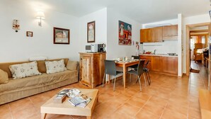 Ein Wohnzimmer mit einer Couch, einem Couchtisch und einem Essbereich mit Stühlen, sowie eine Küche im Hintergrund.