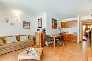 A living room with a sofa, coffee table, and dining area with chairs and a kitchen in the background. - Theo's House (Bardonecchia)
