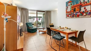 Ein Zimmer mit Esstisch, Stühlen, einem grünen Sessel, einem Holzschrank und einem großen Fenster.