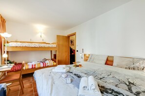 Et hotelværelse med køjeseng, skrivebord med lampe, seng med marmorlignende betræk og et træskab.