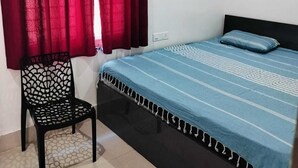 Un dormitorio con cama, una silla y una ventana con cortinas rojas.