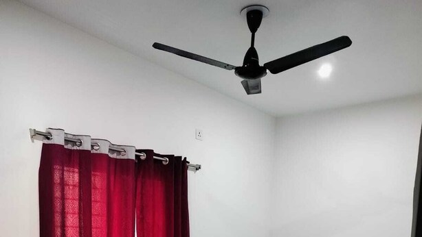 Un dormitorio con cama, ventilador de techo y ventana con cortinas rojas.