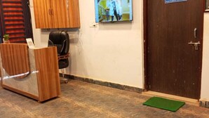 Un área de recepción con un mostrador de madera, una silla de oficina negra, un televisor montado en la pared y una puerta marrón.