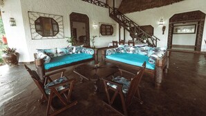 A spacious living area with a high ceiling and a thatched roof. There is a large sofa set with patterned cushions, a coffee table, and wooden chairs. A staircase leads to an upper level. - Spacious 4-bedroom villa in charming Watamu with WiFi (Watamu)