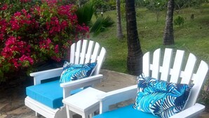 A patio with white Adirondack chairs and blue cushions, surrounded by palm trees and pink bougainvillea. - Spacious 4-bedroom villa in charming Watamu with WiFi (Watamu)