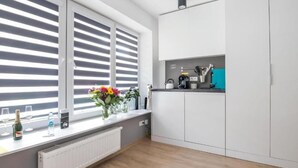 A modern kitchen with white cabinets, a window with blinds, a countertop with kitchenware, and a radiator. - Great Polonia Kraków City Center (Kraków)