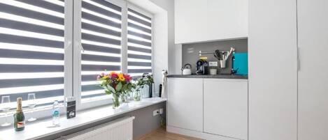 Una cocina moderna con armarios blancos, una ventana con persianas, una encimera con utensilios de cocina y un radiador.