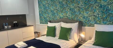 A hotel room with two beds, a kitchenette, and a wall with a leafy pattern.