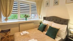 A bedroom with a large bed, a window with curtains, a radiator, a bedside table, and a hanging light fixture. - Great Polonia Kraków City Center (Kraków)
