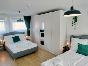 Habitación de hotel con dos camas, un armario amplio, un espejo y una planta colgante.