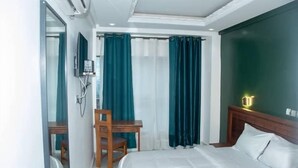 Quarto de hotel com cama, escrivaninha, cadeira e espelho.