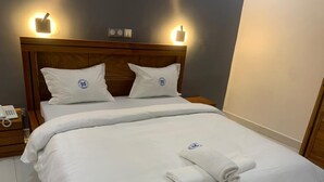 Cama bem arrumada com lençóis e almofadas brancos, cabeceira de madeira e abajures laterais.
