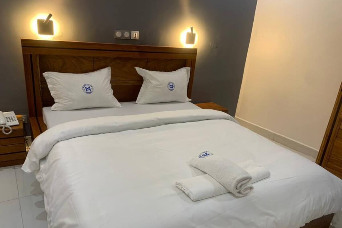 Una cama bien tendida con sábanas y almohadas blancas, un cabecero de madera y lámparas de noche.