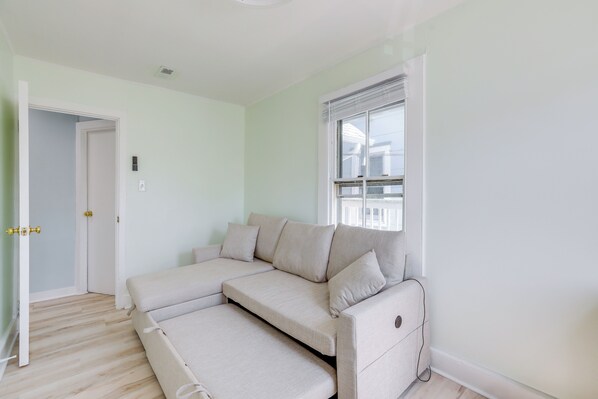 A modern living room with a sectional sofa, a door leading to another room, and a window with blinds. - 2 Blocks to Beach: Sunny Ocean Grove Apartment (Ocean Grove)