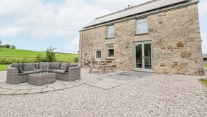 A stone building with a patio area featuring a wicker sofa and a picnic table. - Segrwyd Uchaf (Denbigh)
