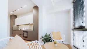 A modern living room with a round wooden table, a white sofa, and a kitchen in the background.