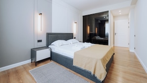 A modern bedroom with a bed, bedside tables, a nightstand, a large mirror, and a wardrobe.